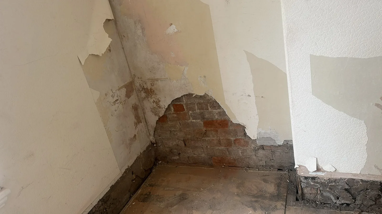 Internal wall partially stripped of plaster to expose brickwork